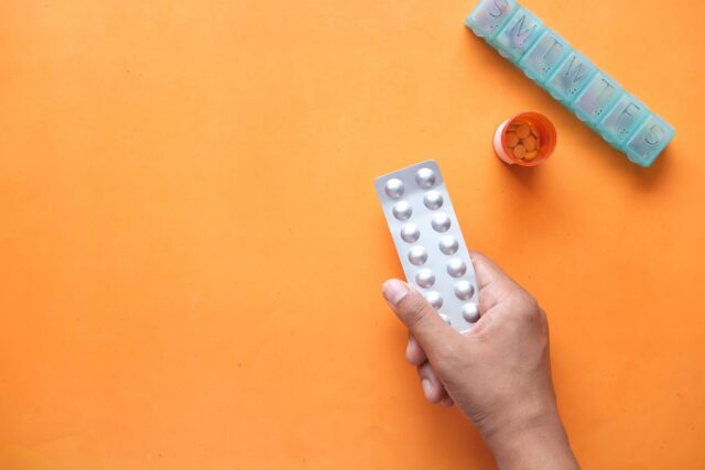 Prospect de medicament desfăcut pe o masă, lângă o folie cu comprimate și o cutie de carton