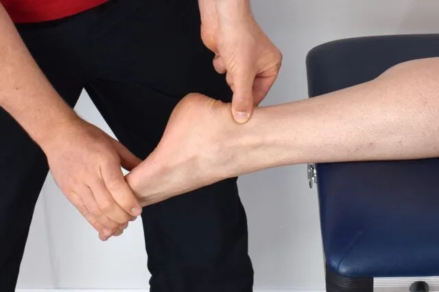 Persoană care face exerciții cu o bandă elastică pentru gleznă, pe un covoraș