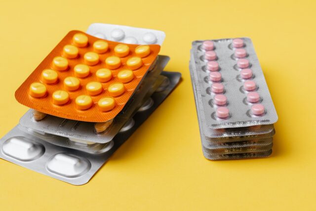 Comprimate, capsule de supliment și o jumătate de grepfrut așezate pe o masă de bucătărie