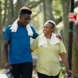 Kinetoterapeut care sprijină un bărbat în vârstă să meargă între bare paralele într-o sală de recuperare