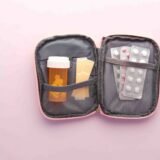 Trusă de prim ajutor deschisă pe o masă, cu bandaje, plasturi, termometru și cutii de medicamente