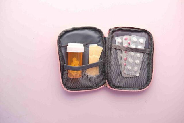 Trusă de prim ajutor deschisă pe o masă, cu bandaje, plasturi, termometru și cutii de medicamente